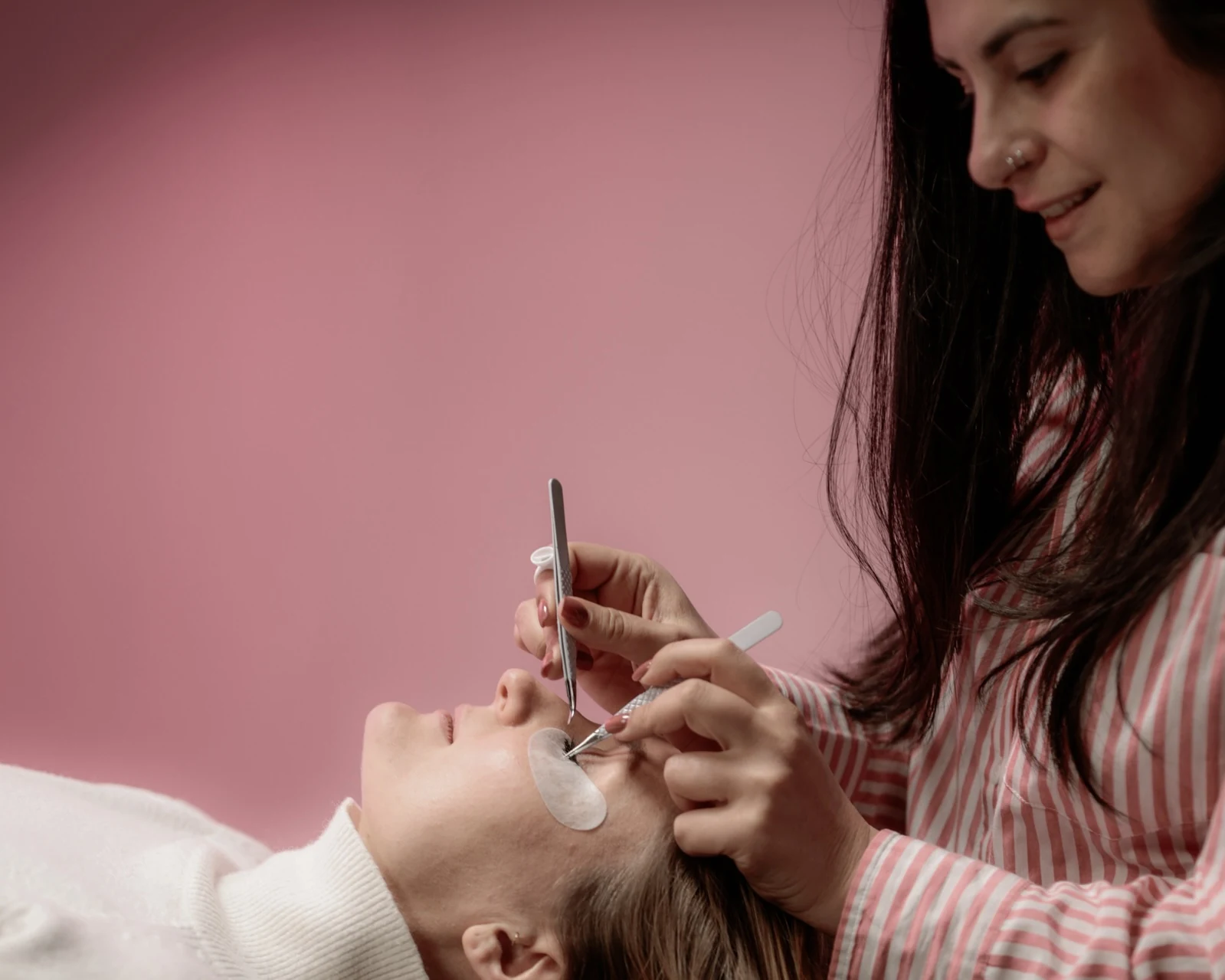 Pose d'extensions de cils chez AlyCare : la praticienne applique une extension à l'aide d'une pince sur l'œil fermé d'une cliente allongée.